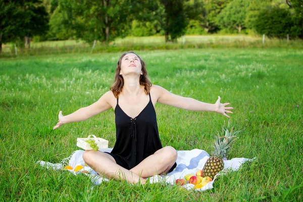 Young woman sitting outdoors in nature and is stretching — Stock Photo, Image