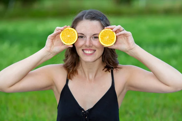 Joven mujer de pie al aire libre y sosteniendo rebanada de naranjas en fr —  Fotos de Stock