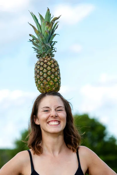 young brunette woman balancing a pineapple on her head
