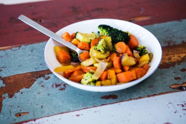 Tahta masada karışık sebzeli beyaz bir tabağın yakın çekimi.