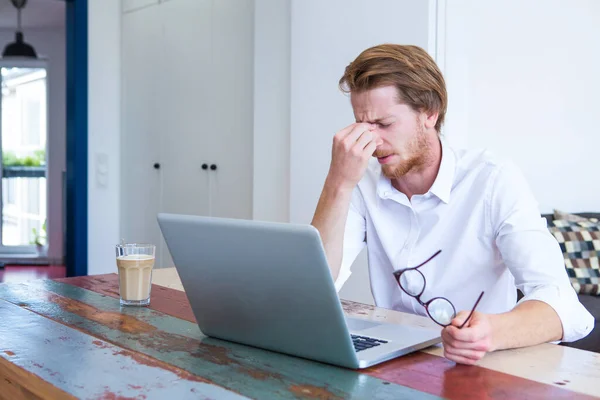 Genç Kızıl Saçlı Adam Dizüstü Bilgisayarıyla Masada Oturuyor Başı Ağrıyor — Stok fotoğraf