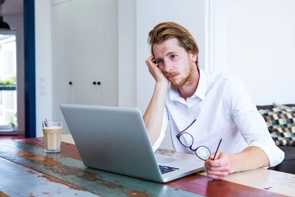 Rusovlasý Mladý Muž Sedí Stolu Svým Laptopem Vypadá Smutně — Stock fotografie