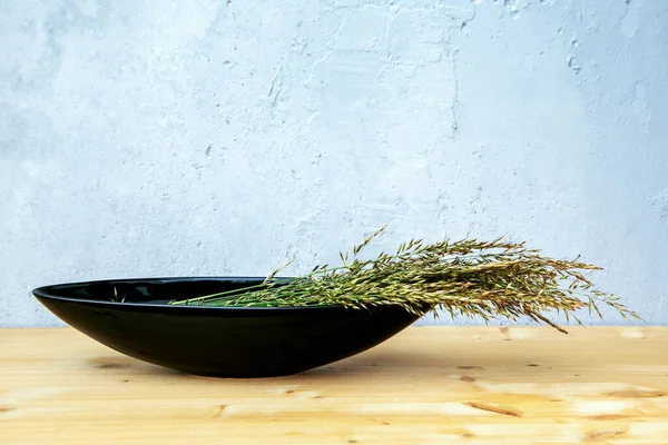 灰色の背景のテーブルの上に草の刃の黒いボウル — ストック写真