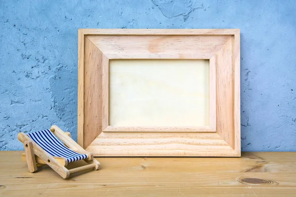 wooden picture frame on table with miniature sun lounger on blue background