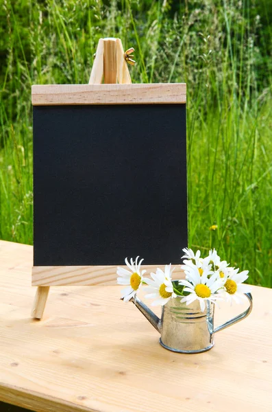 木制桌子上的小黑板 上面有雏菊和迷你浇水 — 图库照片