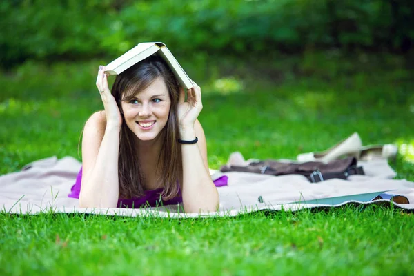 Молодая Брюнетка Лежит Одеяле Парке Держит Книгу Голове — стоковое фото