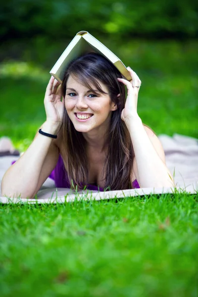 Молодая Брюнетка Лежит Одеяле Парке Держит Книгу Голове — стоковое фото