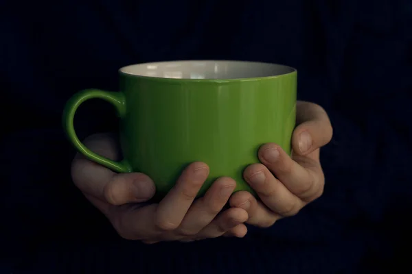 ceramic green cup in hands on a dark background