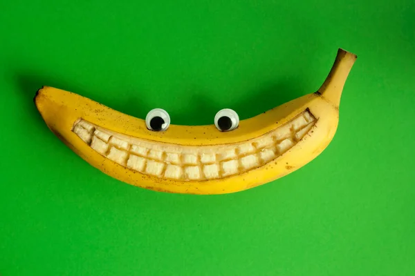 Banana with toy eyes and with a smile against a green background