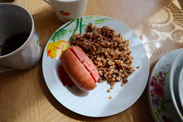 Desayuno en un día soleado de verano gachas de trigo sarraceno y salchichas en un plato —  Fotos de Stock