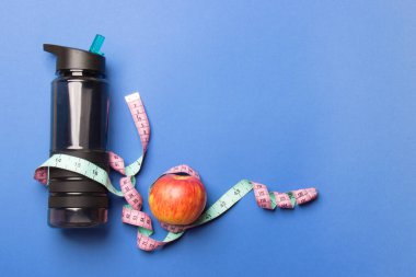 siyah plastik spor şişesi, elma ve santimetre bant mavi arkaplan üzerinde fotokopi alanı ile yatıyor.