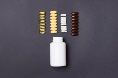 Beyaz vitamin kabı ve siyah renkli kağıt arka planda haplar.
