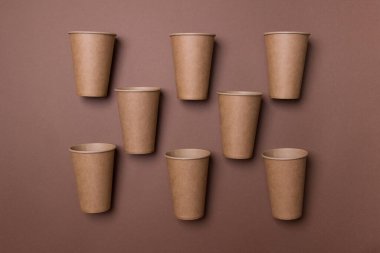 Kahverengi renkli kağıt zemin üzerinde satranç tahtası sırasına göre sekiz kahverengi çevre dostu karton kupa var..