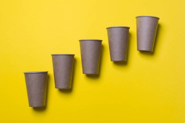 Beş çevre dostu karton bardak sarı renkli kağıdın arka planında köşegen üzerinde yatıyor. Model-up. Yakın plan..