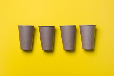 Dört çevre dostu karton bardak sarı renkli kağıdın üzerinde yatıyor. Model-up. Yakın plan. Ekoloji kavramı.