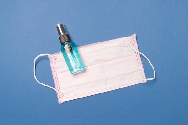 Medical face mask and sanitizer on blue colored paper background.