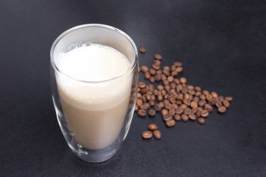 Bir fincan kapuçino ve siyah arka planda kahve tohumu..