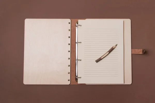 Opened big wooden notebook with pen ready to write on brown colored paper background. Top view.