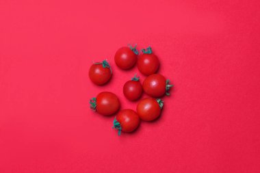Kırmızı renkli kağıttan arka planda küçük bir kırmızı domates grubu.