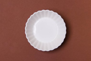 Kahverengi kağıt arka planda boş beyaz tabak.