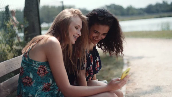 Dos Chicas Jóvenes Usando Teléfono Móvil Mientras Están Sentadas Banco — Foto de Stock