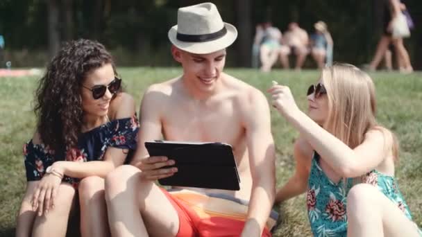 草の上に座っている間彼らのタブレットを探して友人 タブレット コンピューターを使用して友人の幸せな混合民族グループ — ストック動画