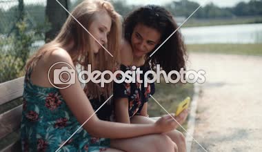 Bir bankta otururken cep telefonuyla iki genç kız.