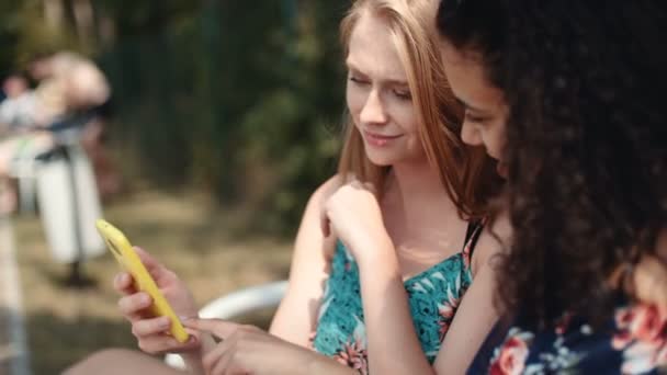 Dos Chicas Jóvenes Usando Teléfono Móvil Mientras Están Sentadas Banco — Vídeo de stock