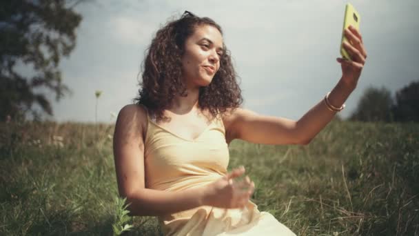 草の上に座って携帯電話で Selfie を取る若い美しい女性 — ストック動画