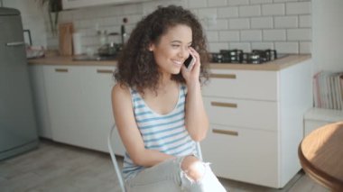 Genç kadın cep telefonuyla bir mutfak.