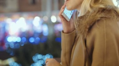 Avrupa Noel piyasasında Smartphone kullanan kadın. Noel, sosyal ağ ve iletişim kavramı. Arka plan bulanık Noel ışıkları.