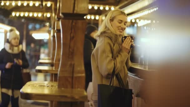 晚上在圣诞市场喝热饮的快乐迷人的女人 — 图库视频影像