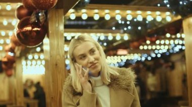 Avrupa Noel piyasasında Smartphone kullanan kadın. Noel, sosyal ağ ve iletişim kavramı. Arka plan bulanık Noel ışıkları.