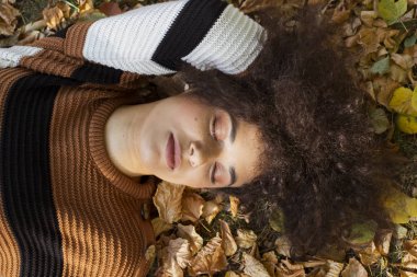 Güneşli parkta sonbahar yaprakları üzerinde uzanan genç Afro-Amerikan kadın..