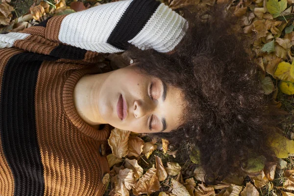 Güneşli parkta sonbahar yaprakları üzerinde uzanan genç Afro-Amerikan kadın..