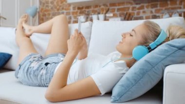 Evde akıllı telefonu ve kulaklığı olan genç bir kadın var..