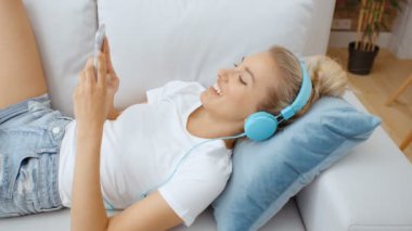 Evde akıllı telefonu ve kulaklığı olan genç bir kadın var..