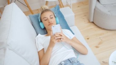 Evde akıllı telefonu ve kulaklığı olan genç bir kadın var..