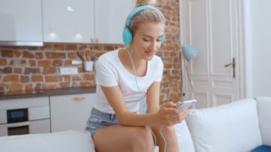 Evde akıllı telefonu ve kulaklığı olan genç bir kadın var..