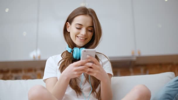自宅でスマートフォンやヘッドフォンを持つ若い女性 — ストック動画