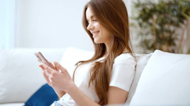 Evde akıllı telefon kullanan genç bir kadın..