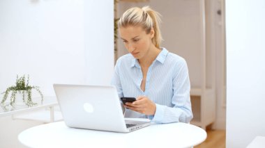 Evde akıllı telefon kullanan genç bir kadın..