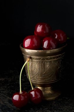 Siyah arka plan üzerine vintage bronz kase kiraz. Metin için yer kopyalayın.