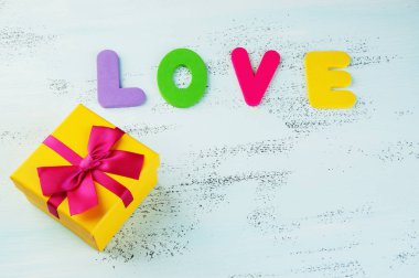 Sarı hediye kutusu yay ve kelime aşk ile eski püskü mavi zemin üzerine çok renkli harflerle kaplı olduğu. Boks gün ve kopya alanı metin için.