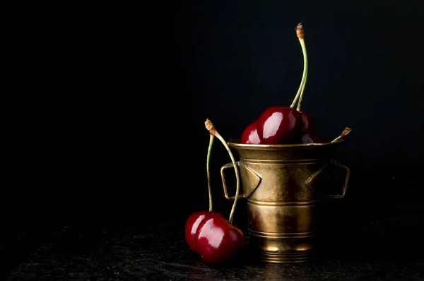 Cherries in vintage bronze bowl on black background. Copy space for text.