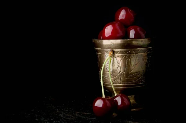 Cherries in vintage bronze bowl on black background. Copy space for text.