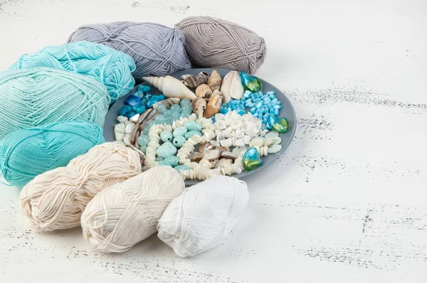 Konu ve boncuk ve kabukları üzerinde eski püskü Beyaz ahşap arka plan gri plaka örgü. Metin için yer kopyalayın.