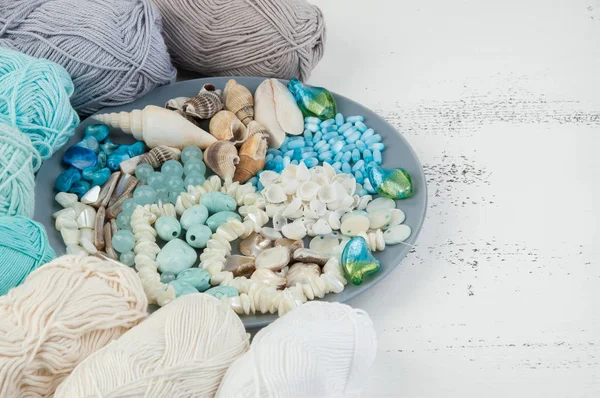 Konu ve boncuk ve kabukları üzerinde eski püskü Beyaz ahşap arka plan gri plaka örgü. Metin için yer kopyalayın.