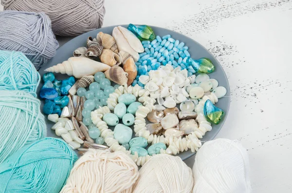 Konu ve boncuk ve kabukları üzerinde eski püskü Beyaz ahşap arka plan gri plaka örgü. Metin için yer kopyalayın.