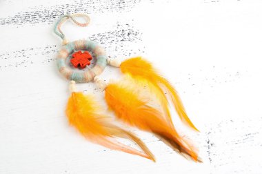 Parlak çok renkli Rüya yakalayıcı turuncu bir haç ve beyaz eski püskü ahşap zemin üzerinde turuncu sarı tüyleri ile. Metin için yer kopyalayın.